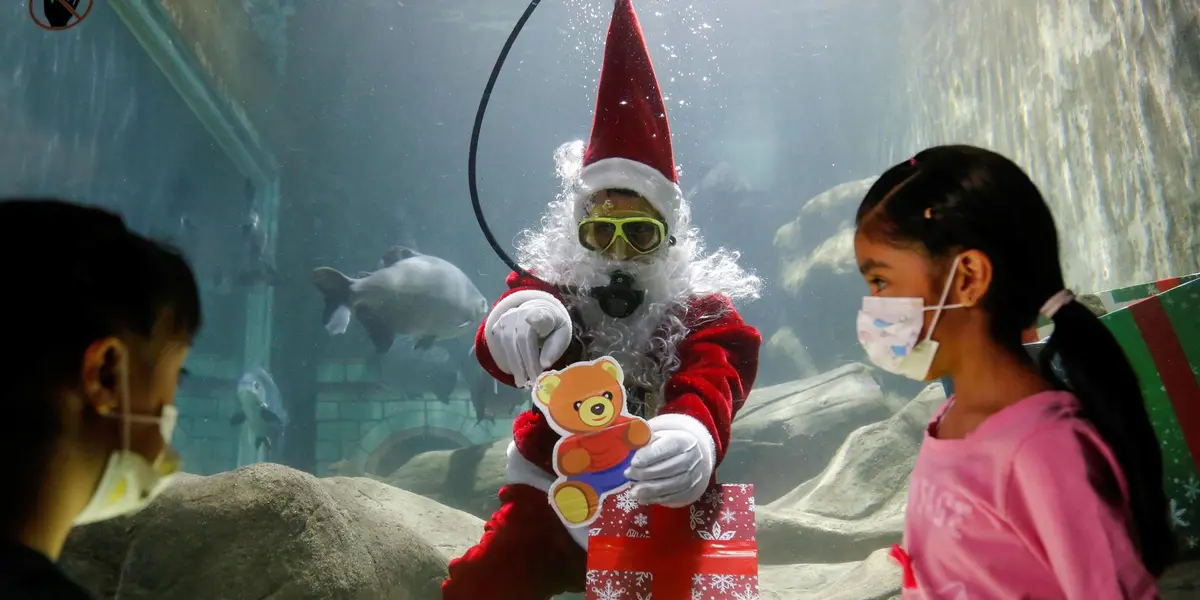 Vestido con su tradicional traje rojo con blanco, el cabello y las barbas blancas del llamado “Santa acuático” se mueven de un lado a otro mientras nada y les muestra los juguetes que carga en una gran caja de regalo.